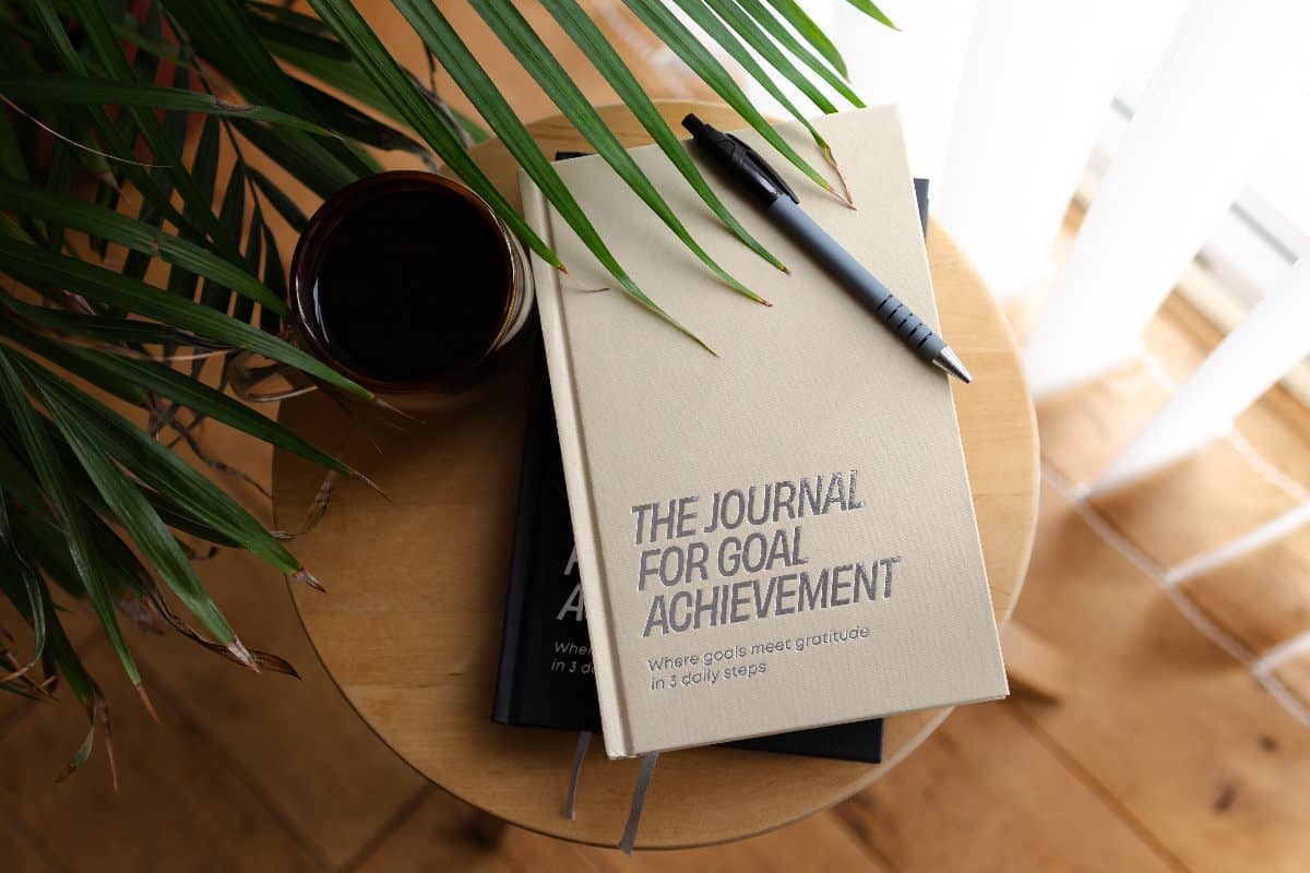 The Journal for Goal Achievement reconnect with your goals The Journal for Goal Achievement on wooden table with pen and coffee, a calming space to reconnect with your goals