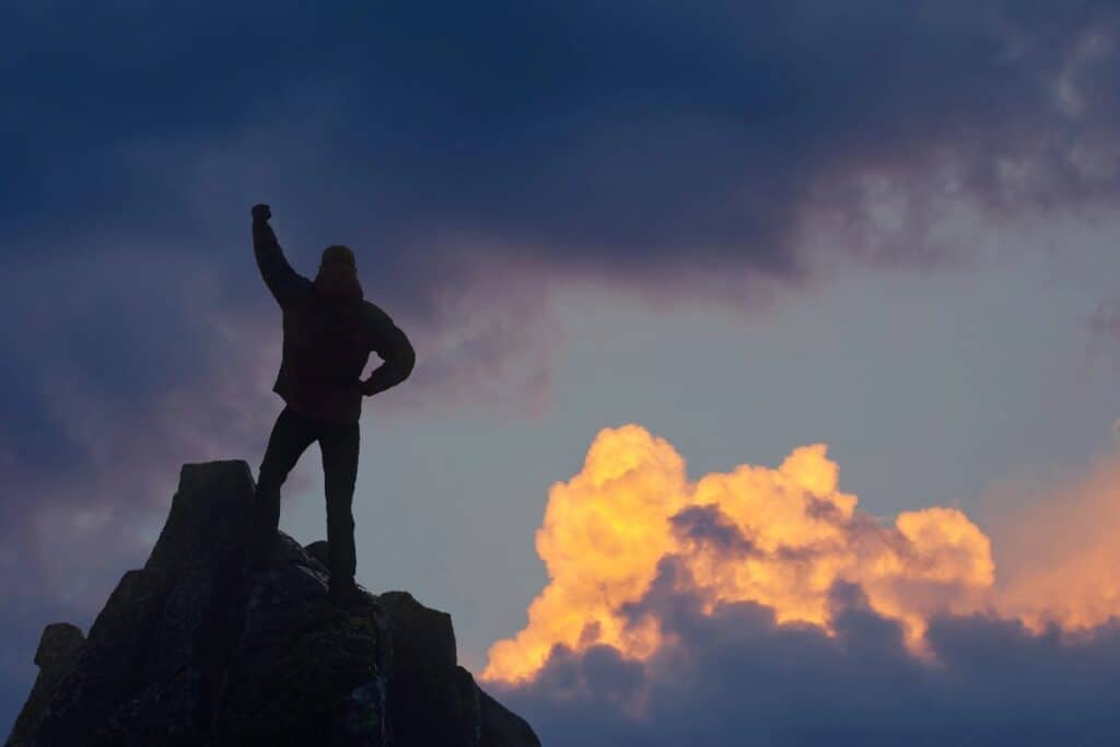 Silhouette of a person standing on a mountain peak at sunset, symbolising the power of an evening routine for success and reflection.