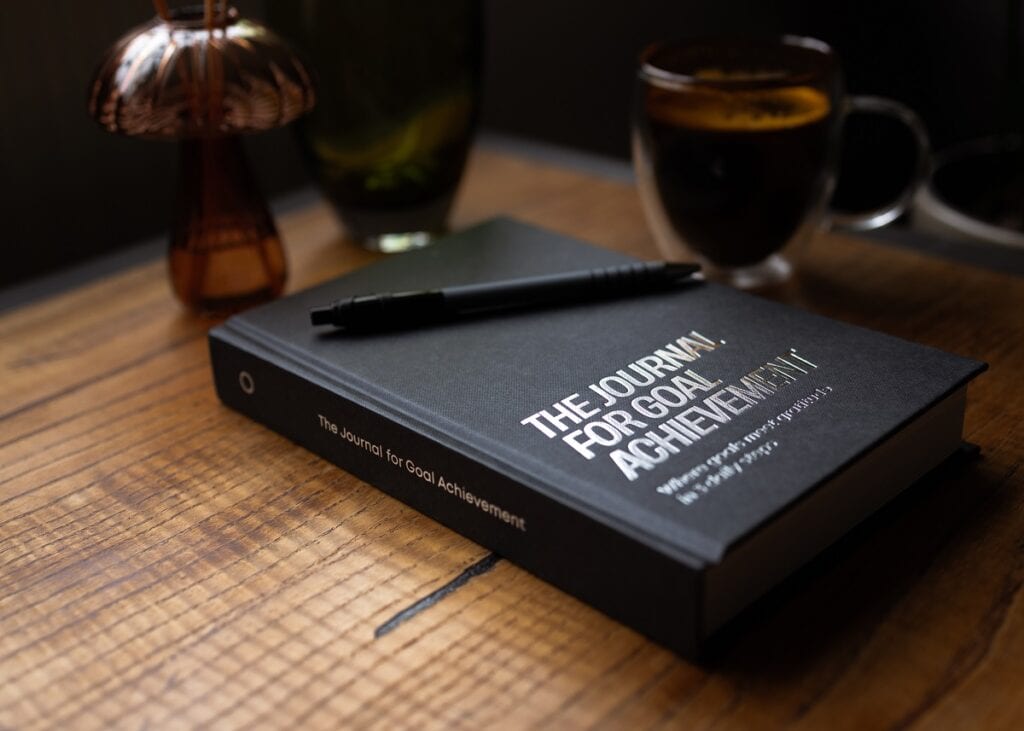The Journal for Goal Achievement closed on a wooden desk with pen and coffee