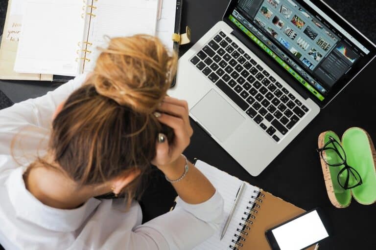 Frustrated woman with head in hands at desk with open planner and laptop