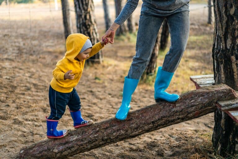 Child walking on log supported by adult, symbolising balance and support for the post about finding the balance