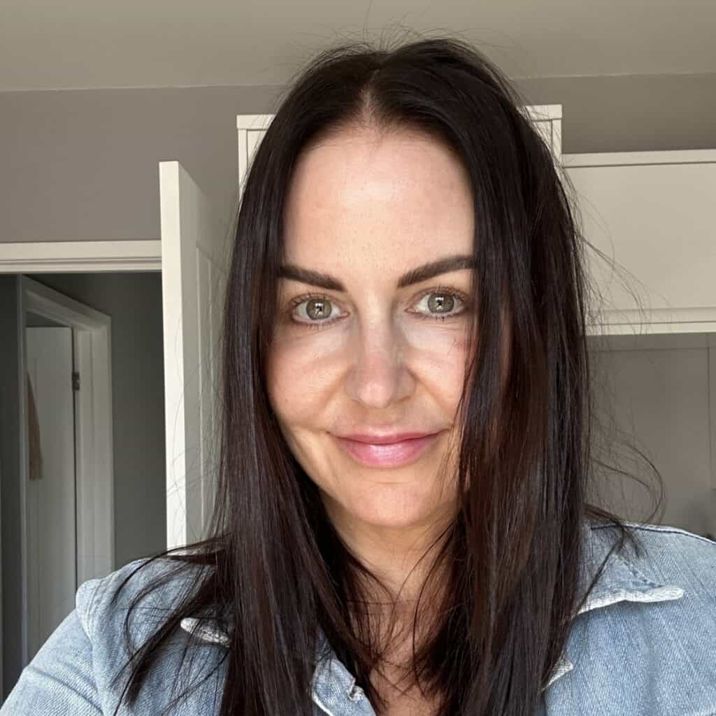 Nicki, Editor and Co-creator of The Journal for Goal Achievement, smiling in natural light wearing a denim jacket