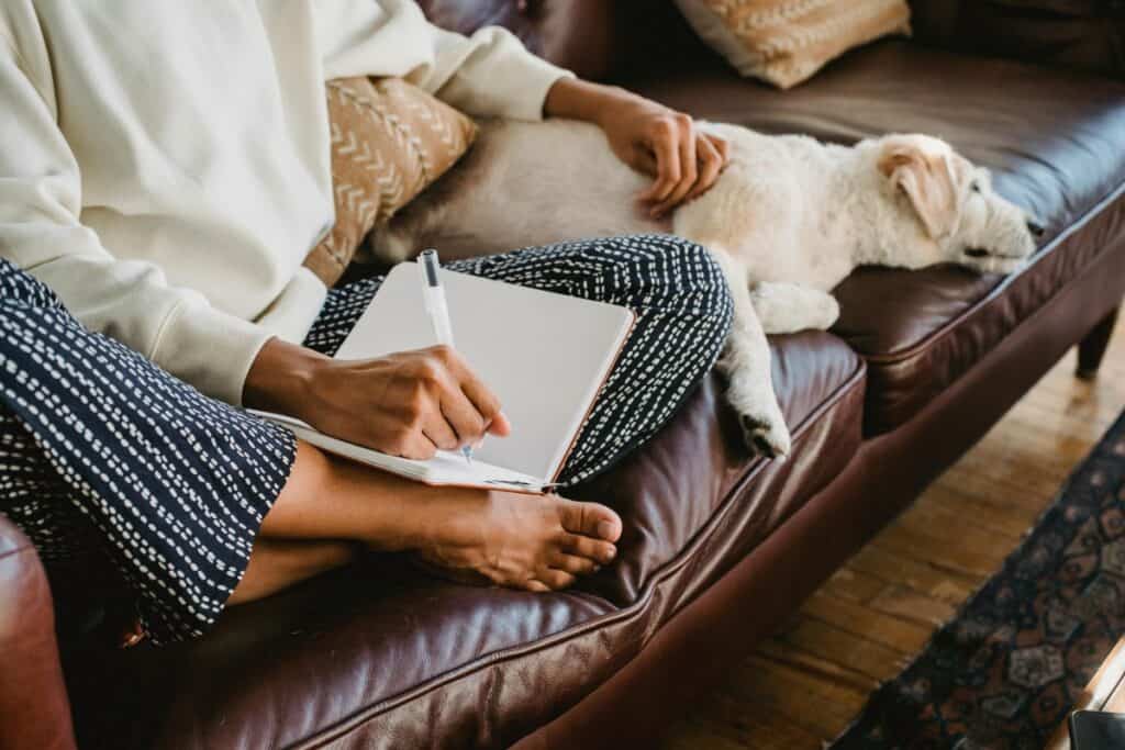 Woman journalling on a sofa with her dog during a relaxed morning routine
