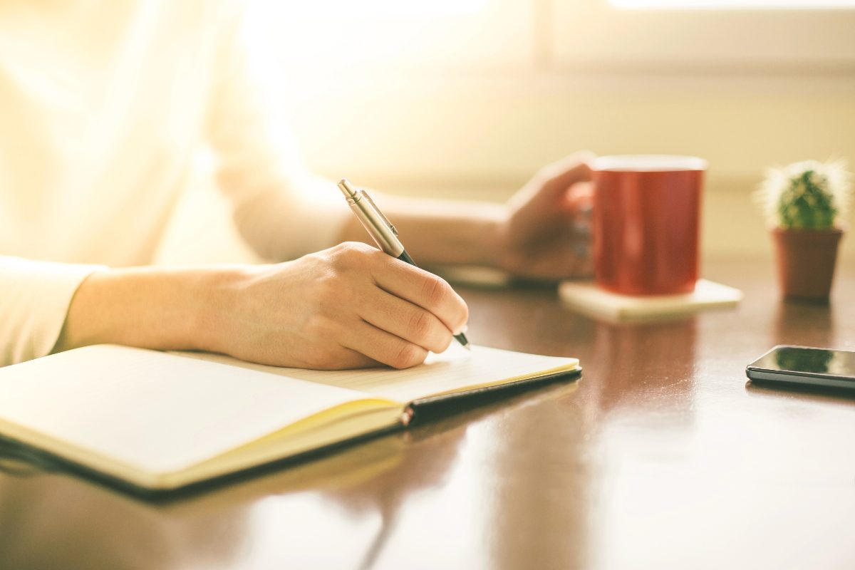 Person writing in a notebook to create a Stop-Doing List and reflect on goal progress.