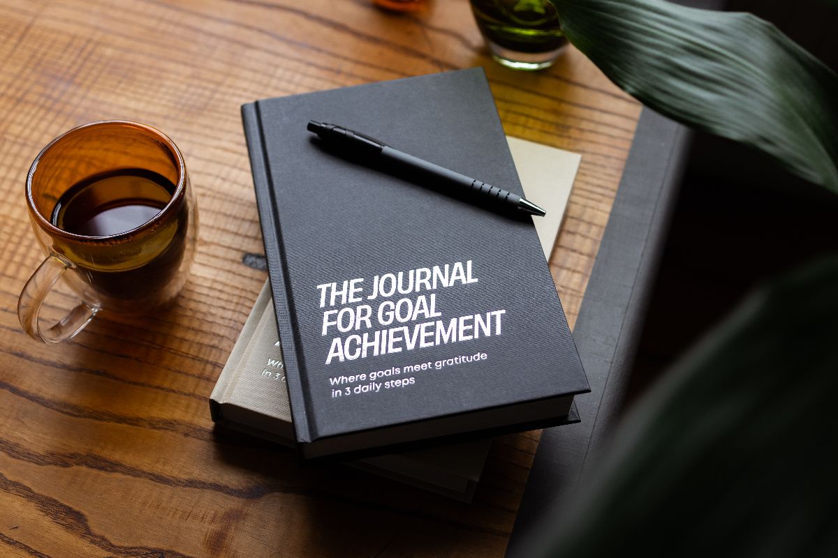 The Journal for Goal Achievement on a wooden desk with coffee, showing a simple daily system for discipline vs motivation.