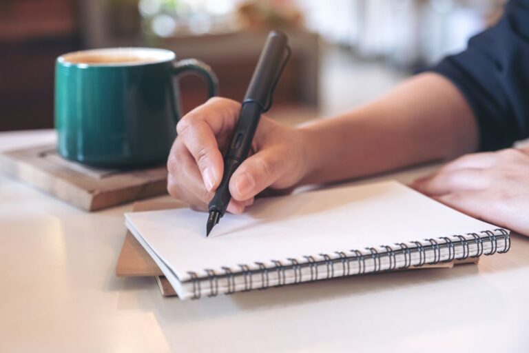 Person writing in a notebook beside a cup of coffee, illustrating the benefits of writing things down.